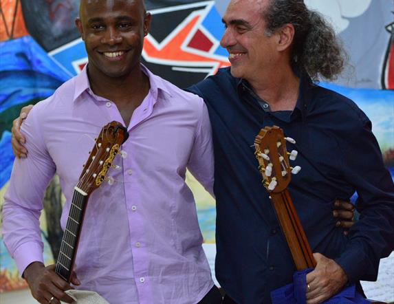 A vibrant photograph shows guitar virtuosos Ahmed Dickinson Cardenas and grammy-nomicated Eduardo Martín with their Spanish guitars smiling at each ot