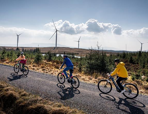 Group in single file on electric bikes on a trail with wind turbines in the background enjoying the Electric Escape experience with Corralea Adventure