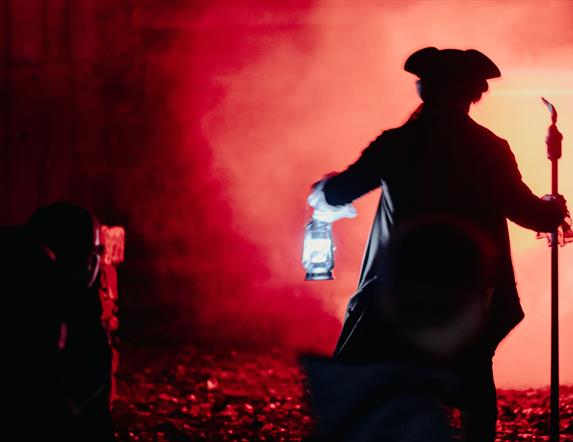 A red background and a man dressed up for halloween holding a torchlight