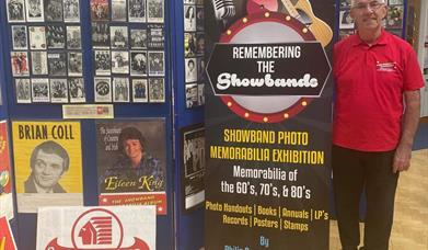 Photo of Philip D'arcy standing beside exhibition title