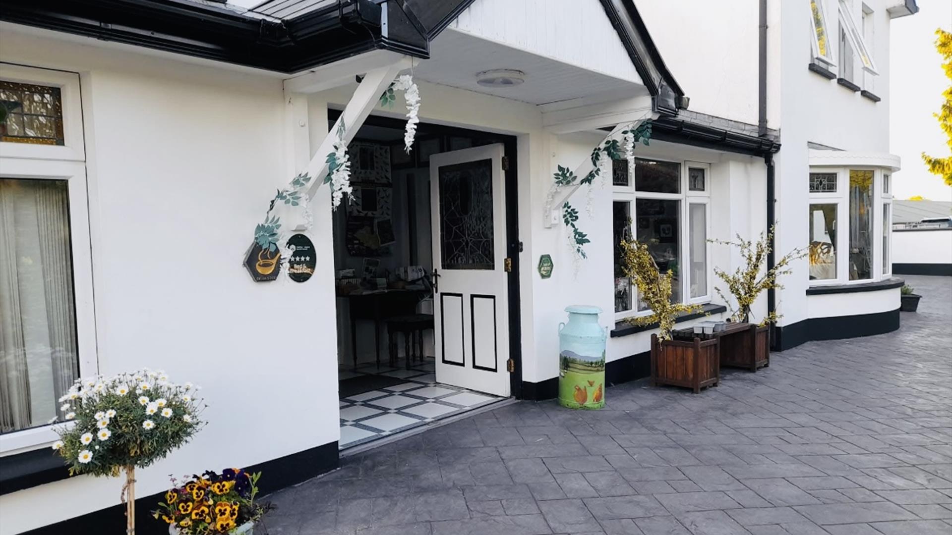 Exterior entrance of Arch House B&B with front doorway with decorative plants either side and a paved driveway.
