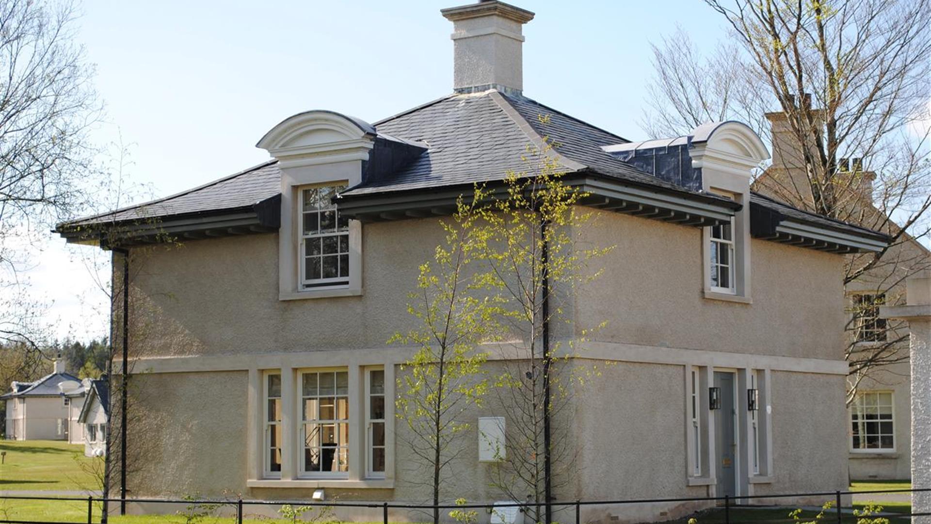 Exterior of two‑storey house with cream exterior, dark roof, and dormer windows