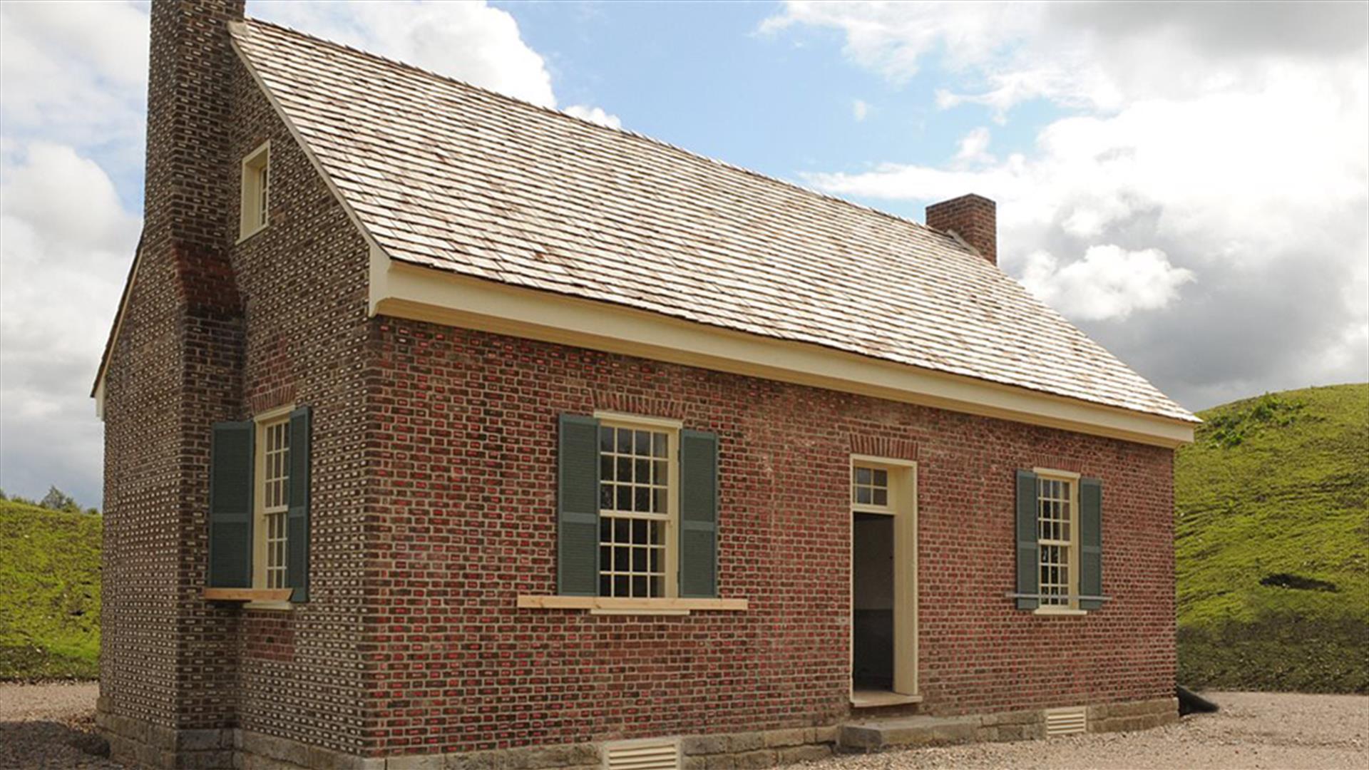 Exterior view of Tennessee Rogan Plantation House. Small  red brick house with green window shutters and steep shingled roof