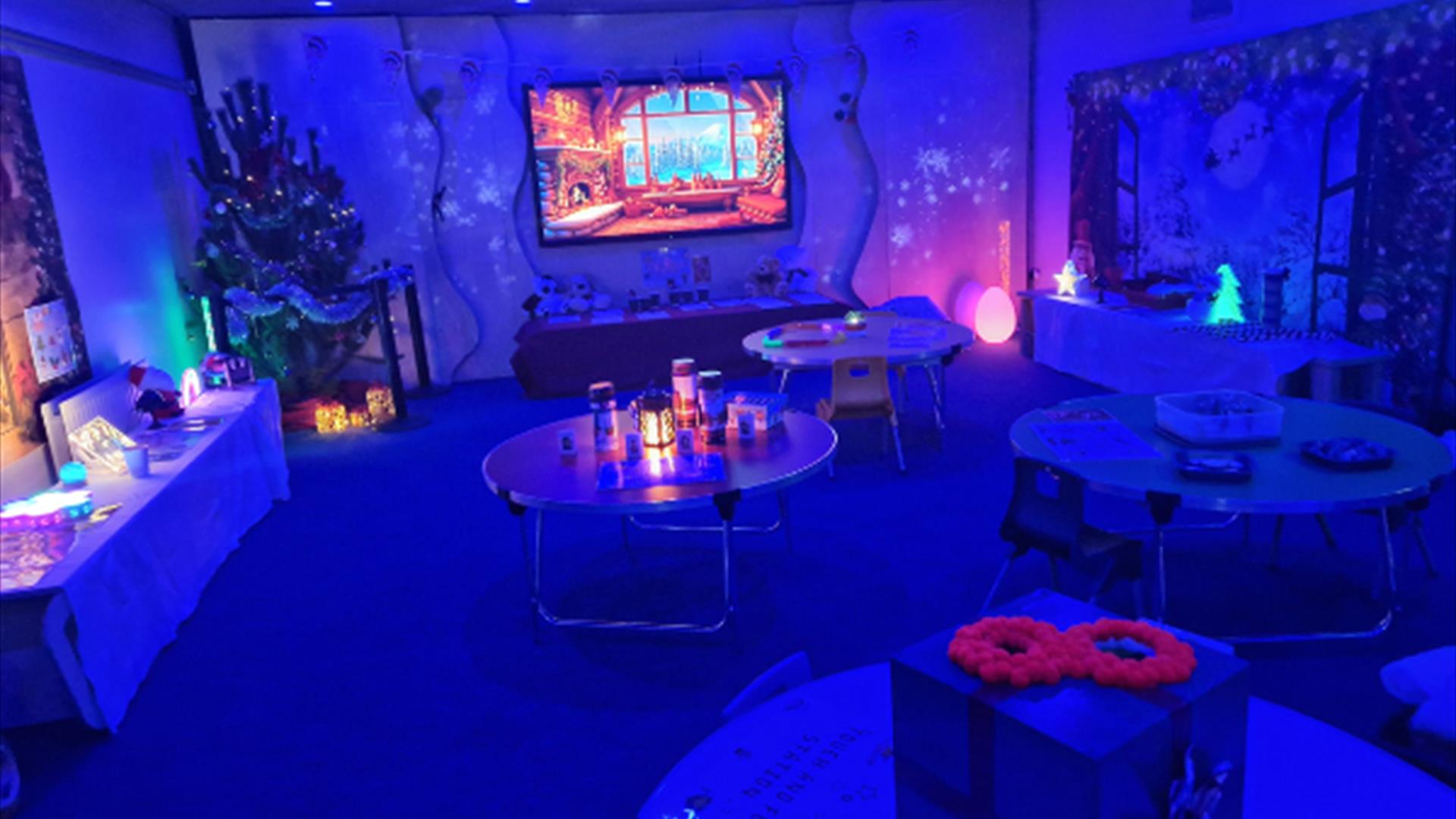 A softly lit sensory room at Marble Arch Caves decorated for Christmas, glowing with calming blue lights. Visitors explore gentle interactive sensory
