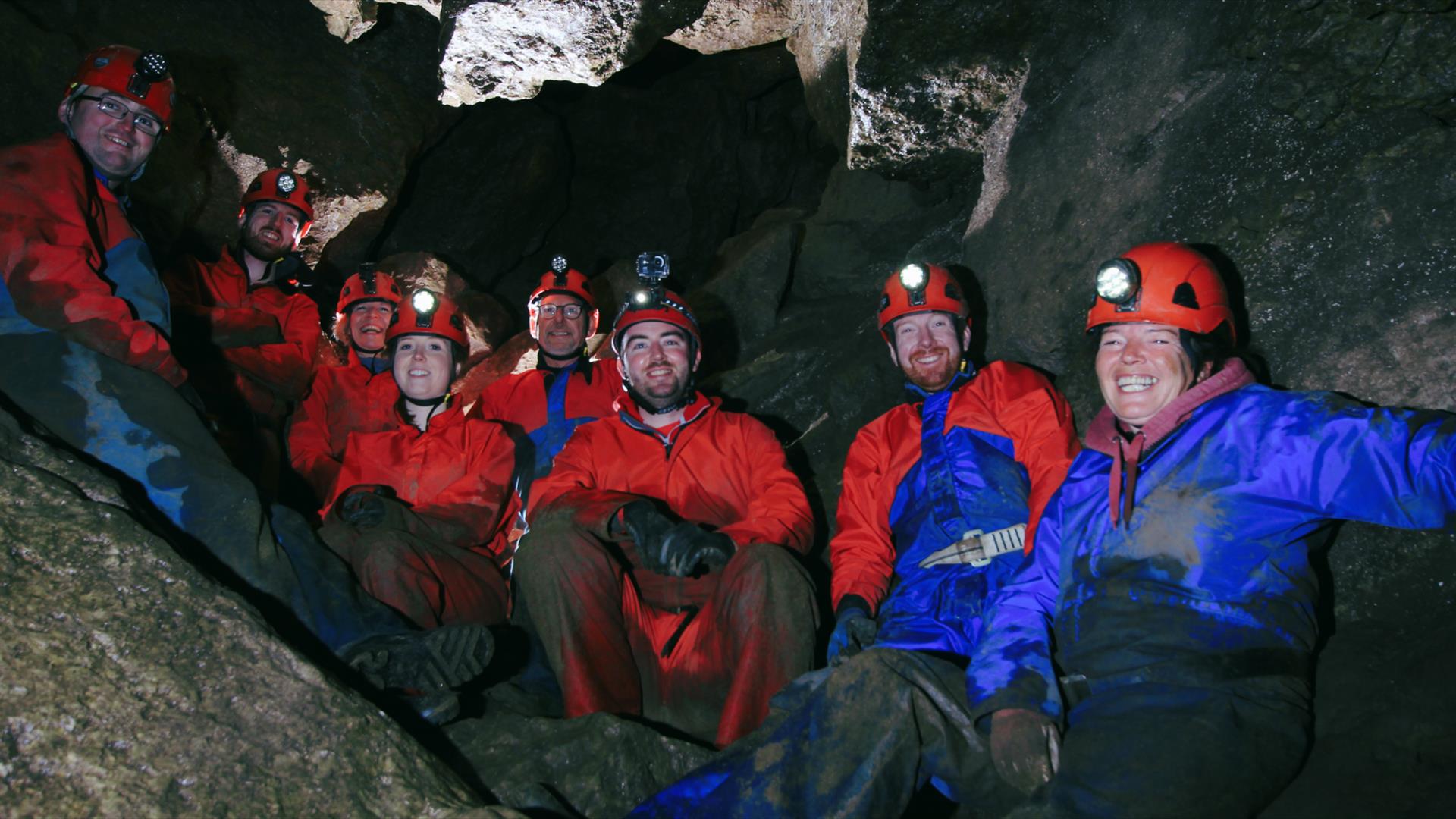 Group of participants wearing helmets and caving gear exploring a wild cave passage during an adventure caving session at Marble Arch Caves.
