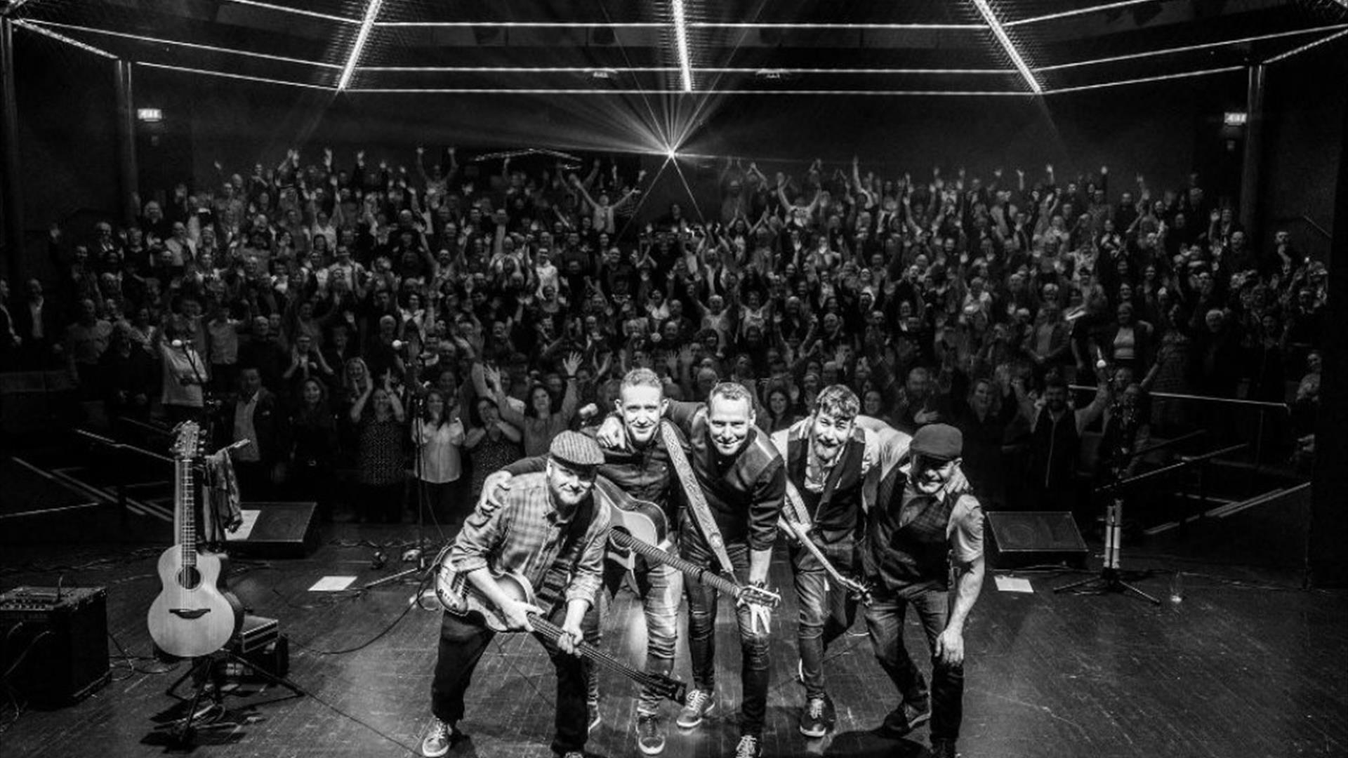 Black and white image of The Highstool Prophets on stage with the audience behind them shining phone lights.