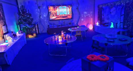 A softly lit sensory room at Marble Arch Caves decorated for Christmas, glowing with calming blue lights. Visitors explore gentle interactive sensory