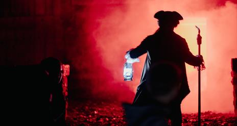 A red background and a man dressed up for halloween holding a torchlight