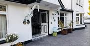Exterior entrance of Arch House B&B with front doorway with decorative plants either side and a paved driveway.