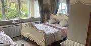 Guest bedroom with double bed and a day bed soft furnishings, light grey curtains, a large window overlooking greenery.
