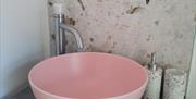 A pink sink in front of a marble wall.