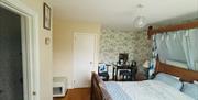 Guest bedroom with King bed, blue and white bedding, floral wallpaper, a small desk and chair, and a doorway leading to an en‑suite bathroom.
