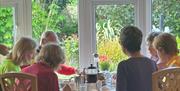Guests enjoying breakfast together at a dining table inside Arch House B&B with large windows overlooking a garden.