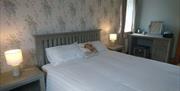 Photograph of a king size bed, made up with white bedding and a decorative cushion. There is a bedside table on both sides of the bed and a table lamp