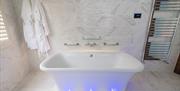 tiled bathroom with bath, floor lighting, hanging robes and towel rack radiator