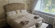 Twin guest room with neutral décor and soft furnishings. A chandelier, and a large window with vertical blinds.