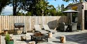 Outdoor patio with lounge chairs, fire pit, barbecue, and covered dining area enclosed by wooden fencing.