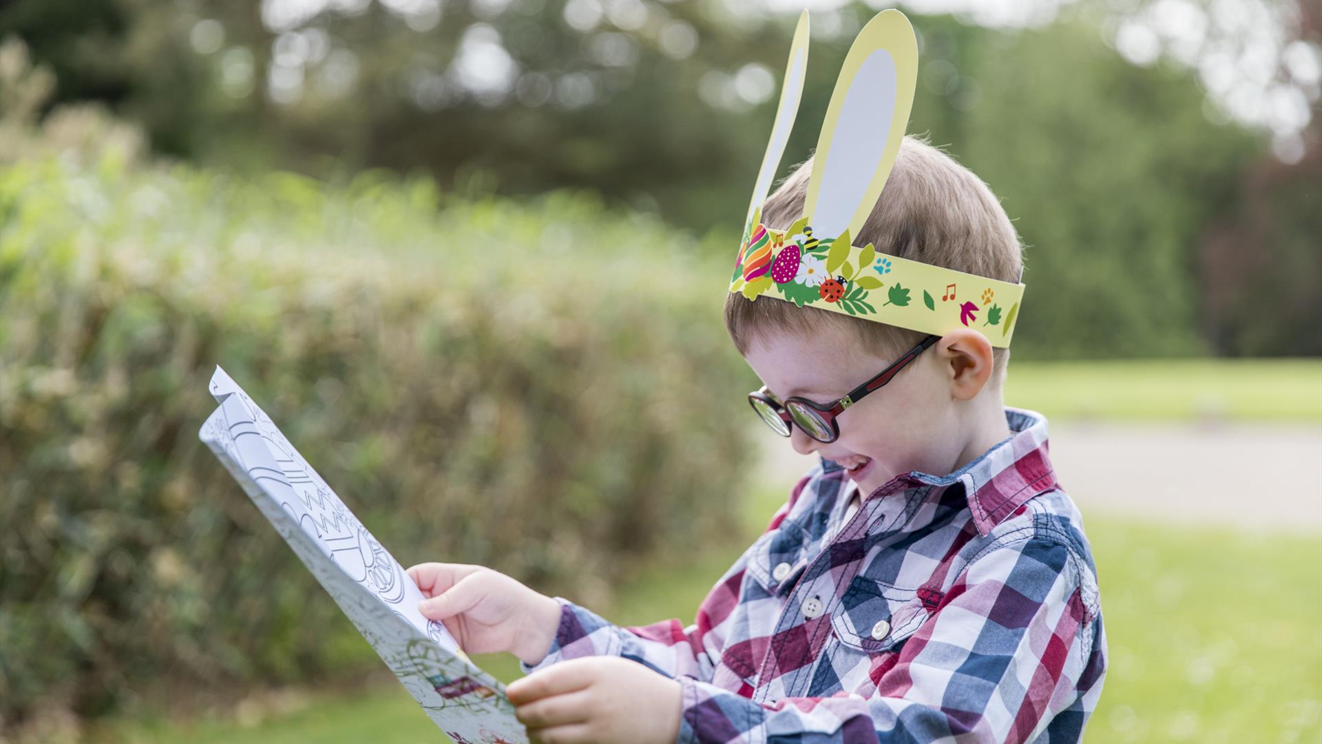A young boy wearing bunny ears reading an Easter trail map