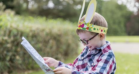 A young boy wearing bunny ears reading an Easter trail map