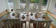 A table set for breakfast with four chairs, two either side. Patio doors behind the table which looks out over the garden with a wooden table and chai