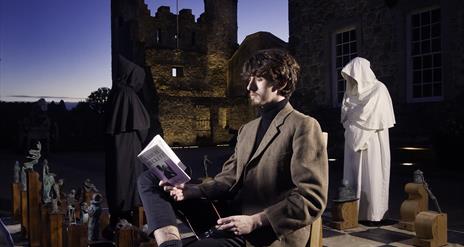 Beckett Festival - image of young man reading Beckett verse by the Isle of Enniskillen Beckett Chess set.